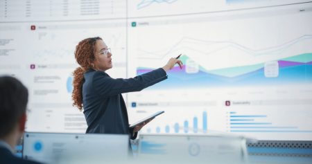 female executive stands in front of a bank of screens showing various risk dashboards