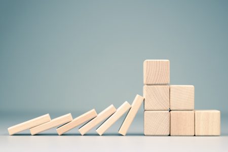 supply chain resilience: a stack of fallen dominos is blocked by a solid wall of blocks.