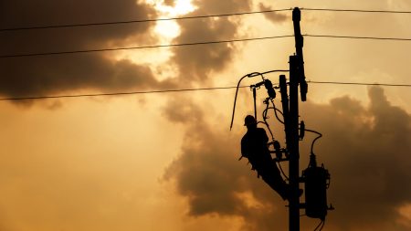 The silhouette of a power lineman climbing on an electric pole with a transformer installed. And replacing the damaged hotline clamp, bail clamp, dropout and surge arrester that causes a power failure.