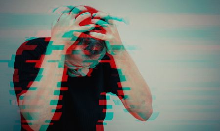 A stressed man standing near a wall and covering his face.