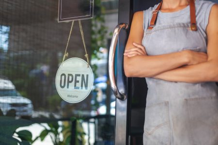 US SBA launches business resilience guide for small businesses A small business owner stands next to an Open sign to show the concept of business resilience