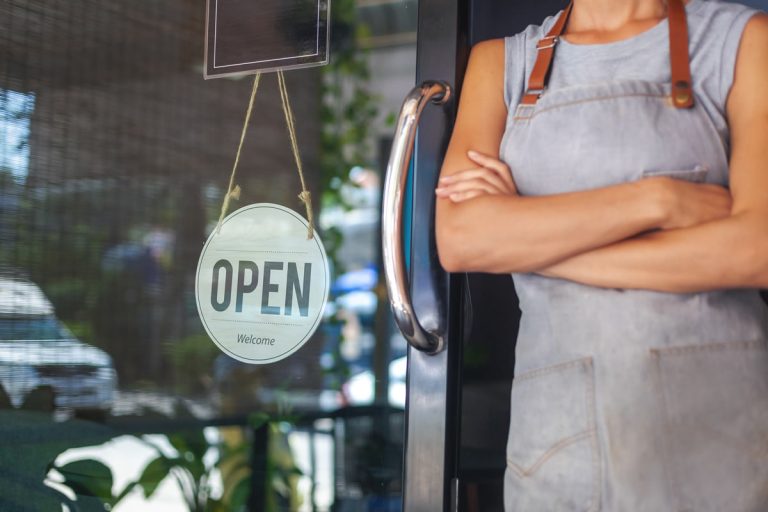 A small business owner stands next to an Open sign to show the concept of business resilience