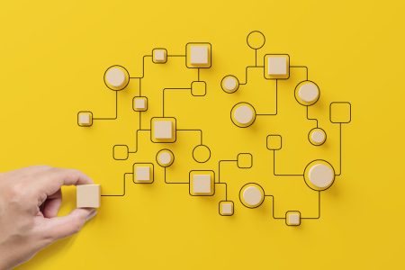 Hand holding wooden cube block arranging a system on a yellow background