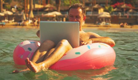 Working from anywhere: a business man works on his laptop while floating in a ring in the sea.