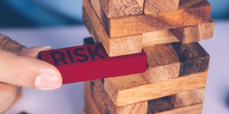 A hand pulls a block labelled Risk from a tower of bricks.