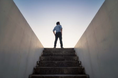 A business man emerges from a flight of stairs into a bright horizon.