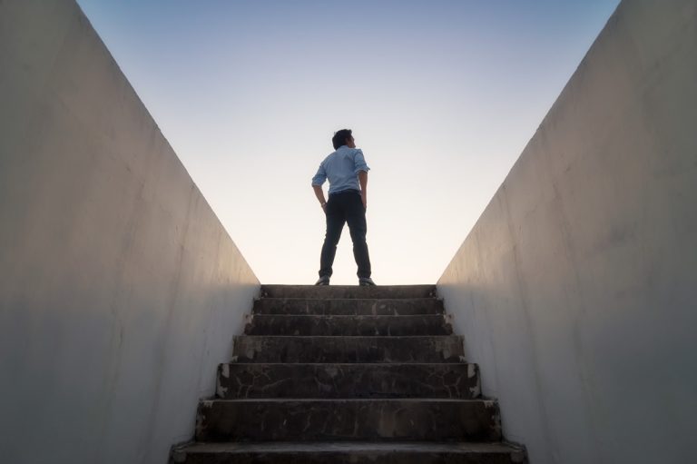 A business man emerges from a flight of stairs into a bright horizon.