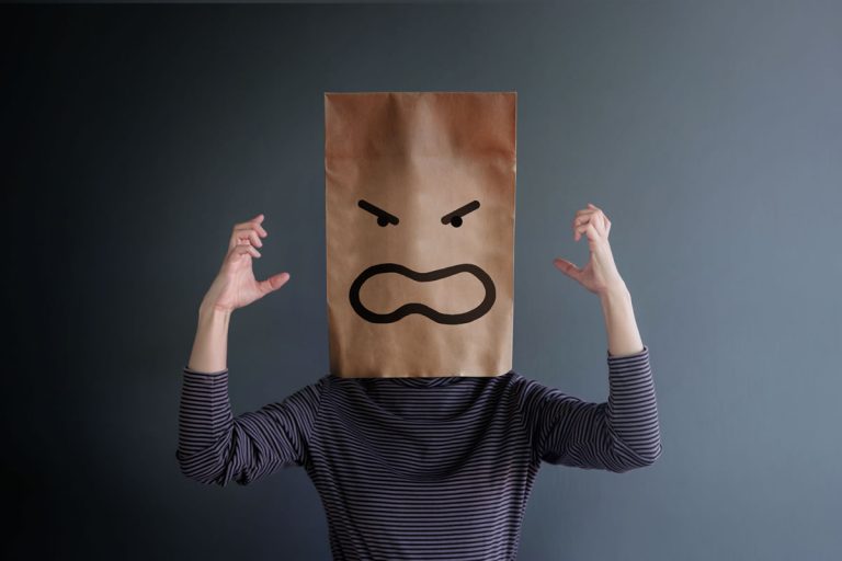 A woman wearing a paper bag on her head with an angry face drawn on it in black marker pen.
