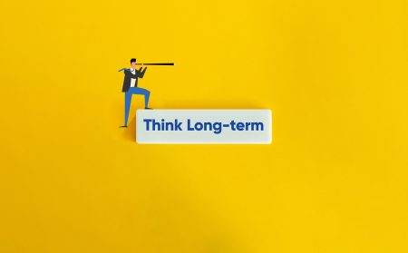 A business person looks through a telescope above a text block stating Think long term.
