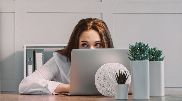 A female worker looks over the top of her laptop to make sure no-one can see what she is doing.