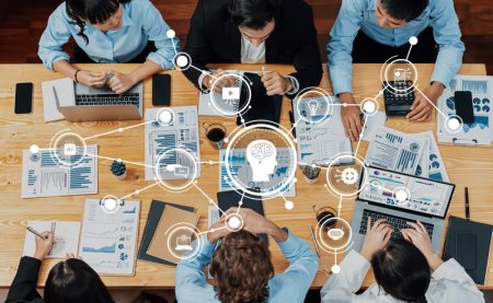 An overhead picture of a team of business people working on a number of documents and using Gen AI to analyse them.