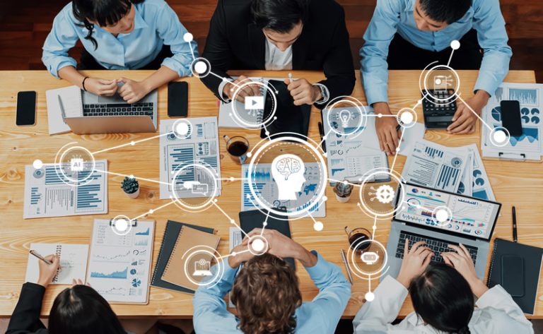 An overhead picture of a team of business people working on a number of documents and using Gen AI to analyse them.