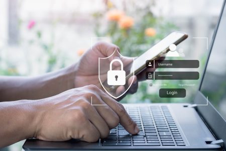Hands holding a mobile phone and entering a verification code on a laptop.