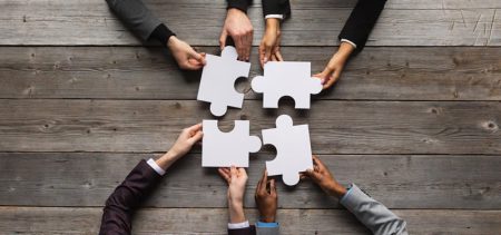Hands bringing four white jigsaw pieces together to illustrate creating an organizational structure.