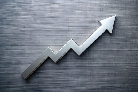 Silver metallic arrow graph trending upwards on a textured grey wooden surface.