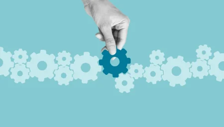 A hand slots a dark blue cog into a line of grey cogs showing the concept of the centrality of culture to cybersecurity.