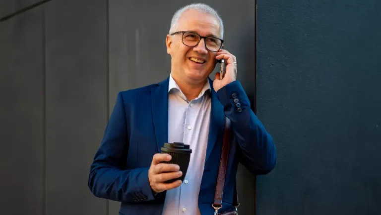 Mature businessman smiling talking on smartphone drinking coffee.
